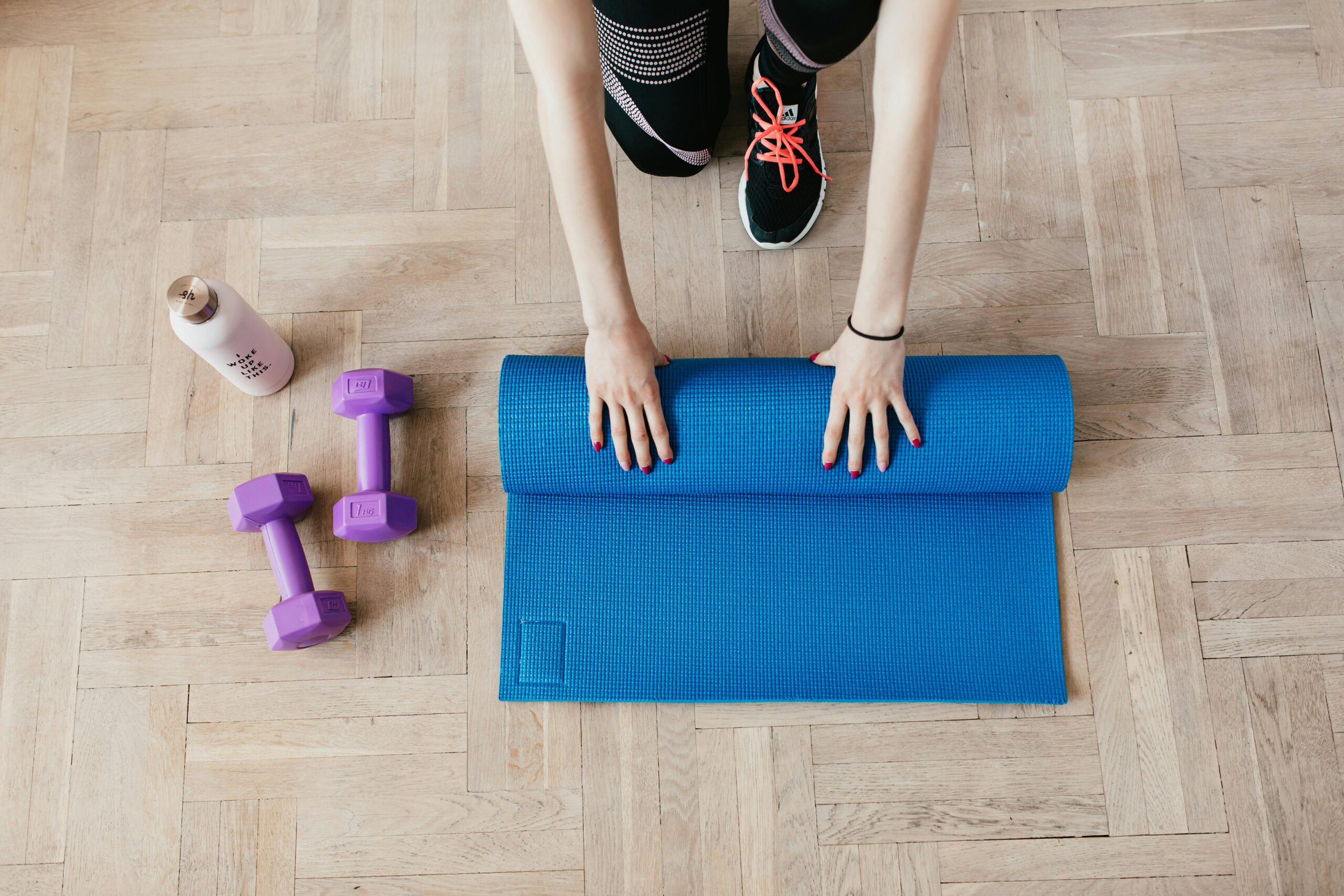 woman rolling up blue yoga mat next to weights and a water bottle 