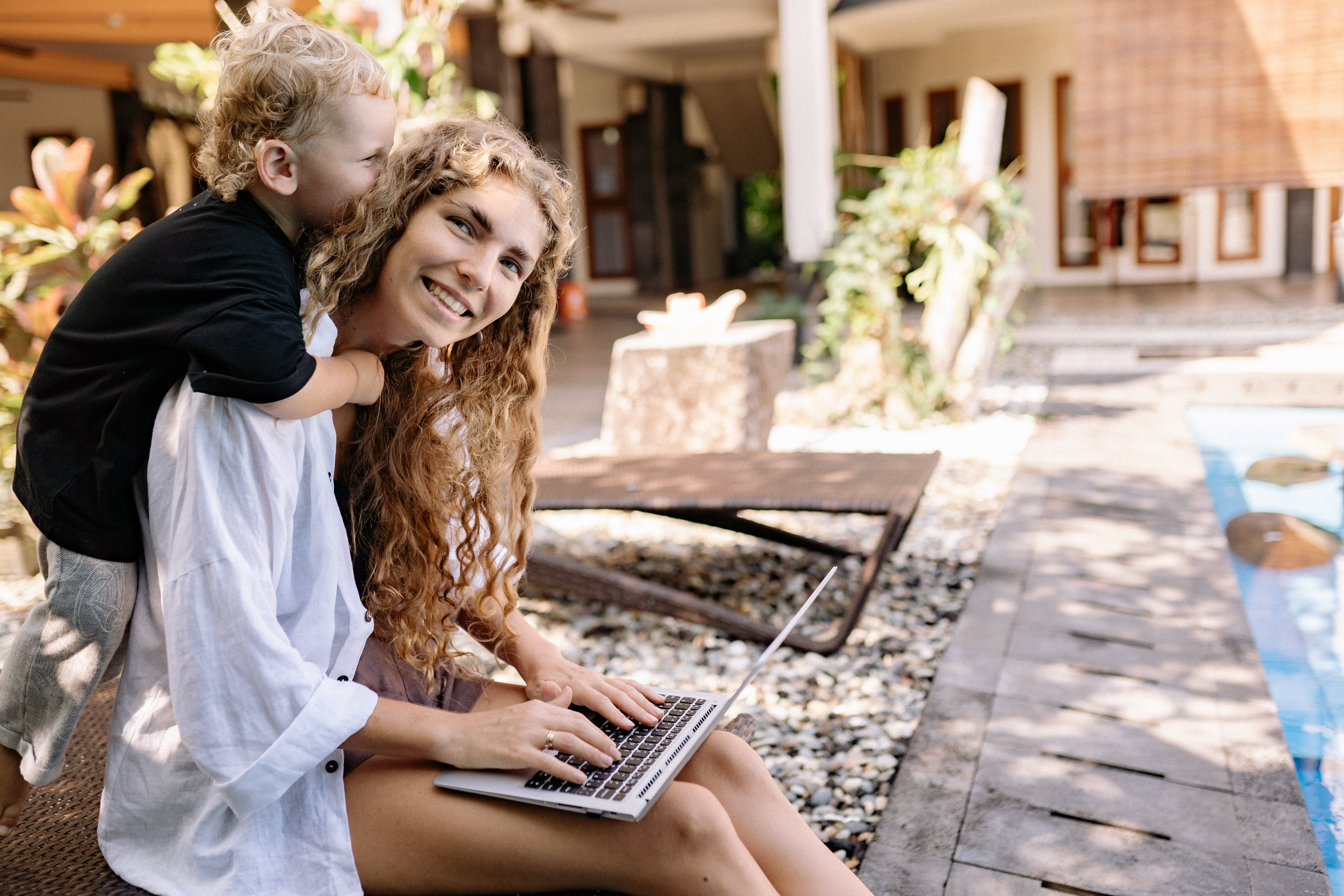 smiling mom being hugged by son from behind while she types on laptop